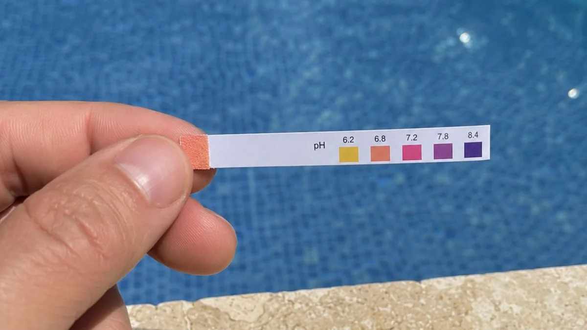 Bandelette test pH affichant 6.8 au bord d'une piscine — échelle colorimétrique de 6.2 à 8.4 pour diagnostic pH trop bas