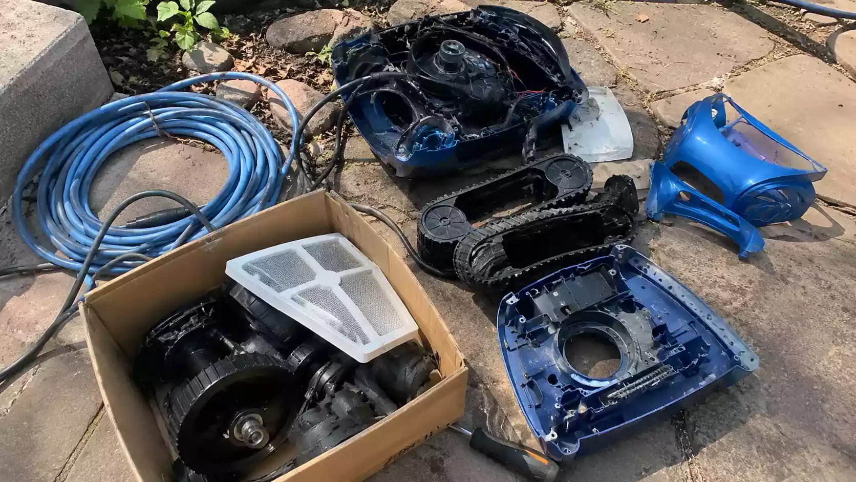 Robot piscine Zodiac démonté avec ses pièces détachées : coque, chenilles, roues, filtre et câble