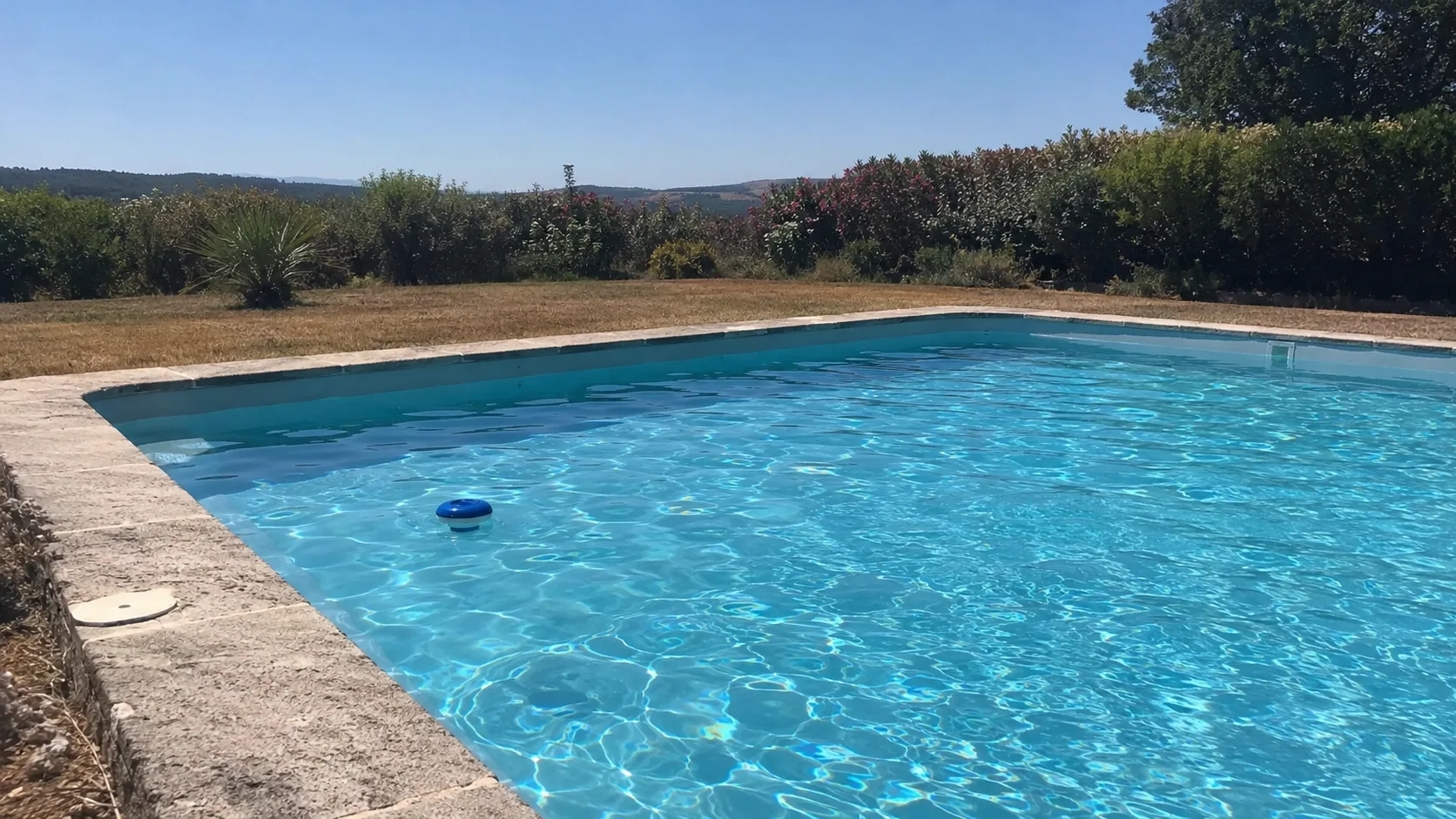 Piscine extérieure à l’eau claire par forte chaleur, pelouse grillée et collines dans le sud de la France