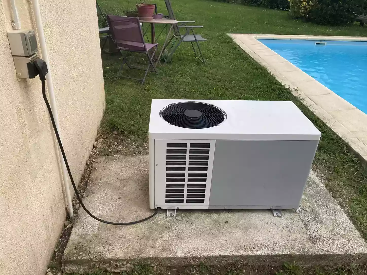 Pompe à chaleur de piscine installée au bord d'un bassin, prise électrique et compteur visibles