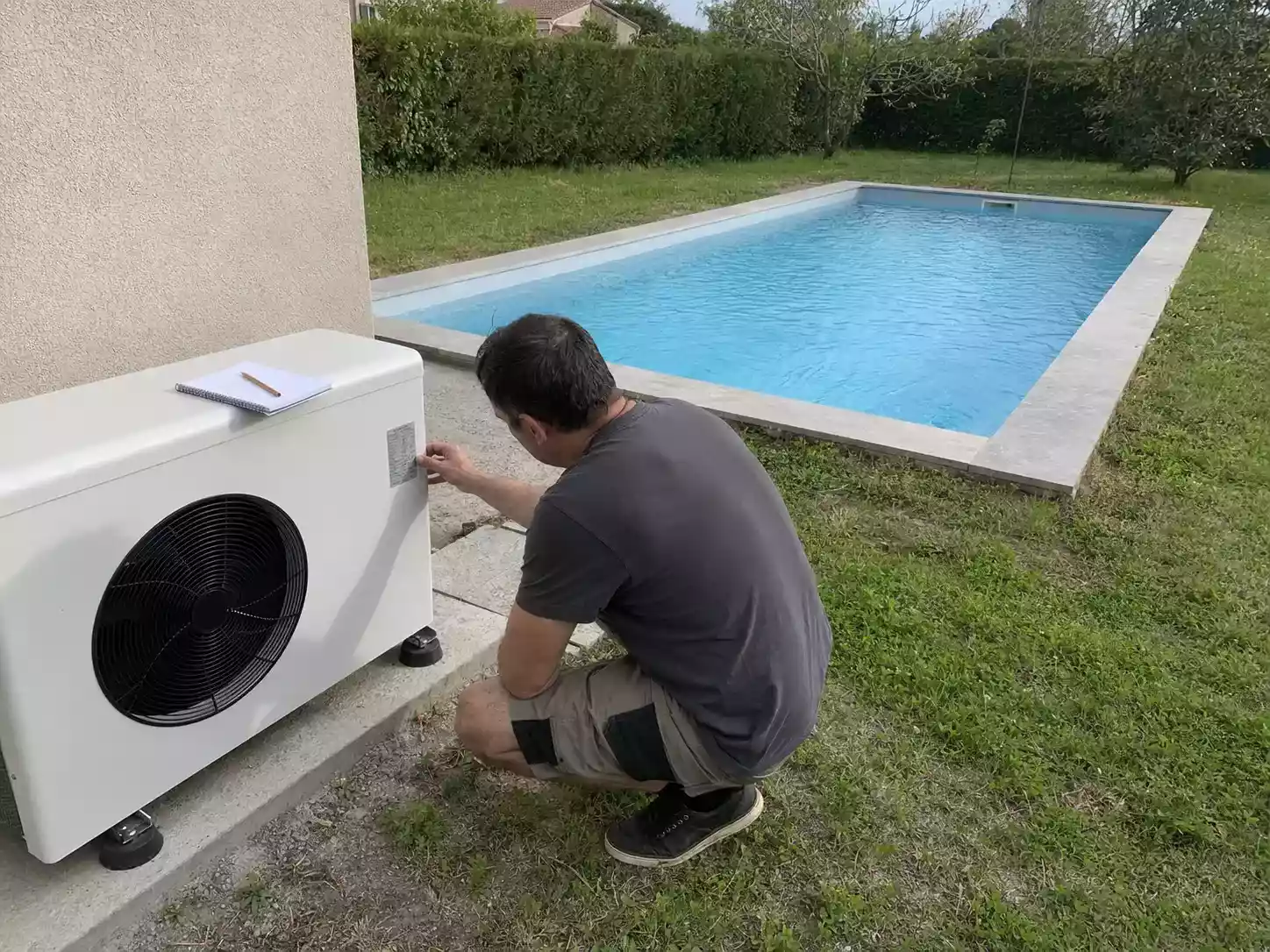 Propriétaire lisant la plaque signalétique d'une pompe à chaleur de piscine, bassin 8x4 en arrière-plan