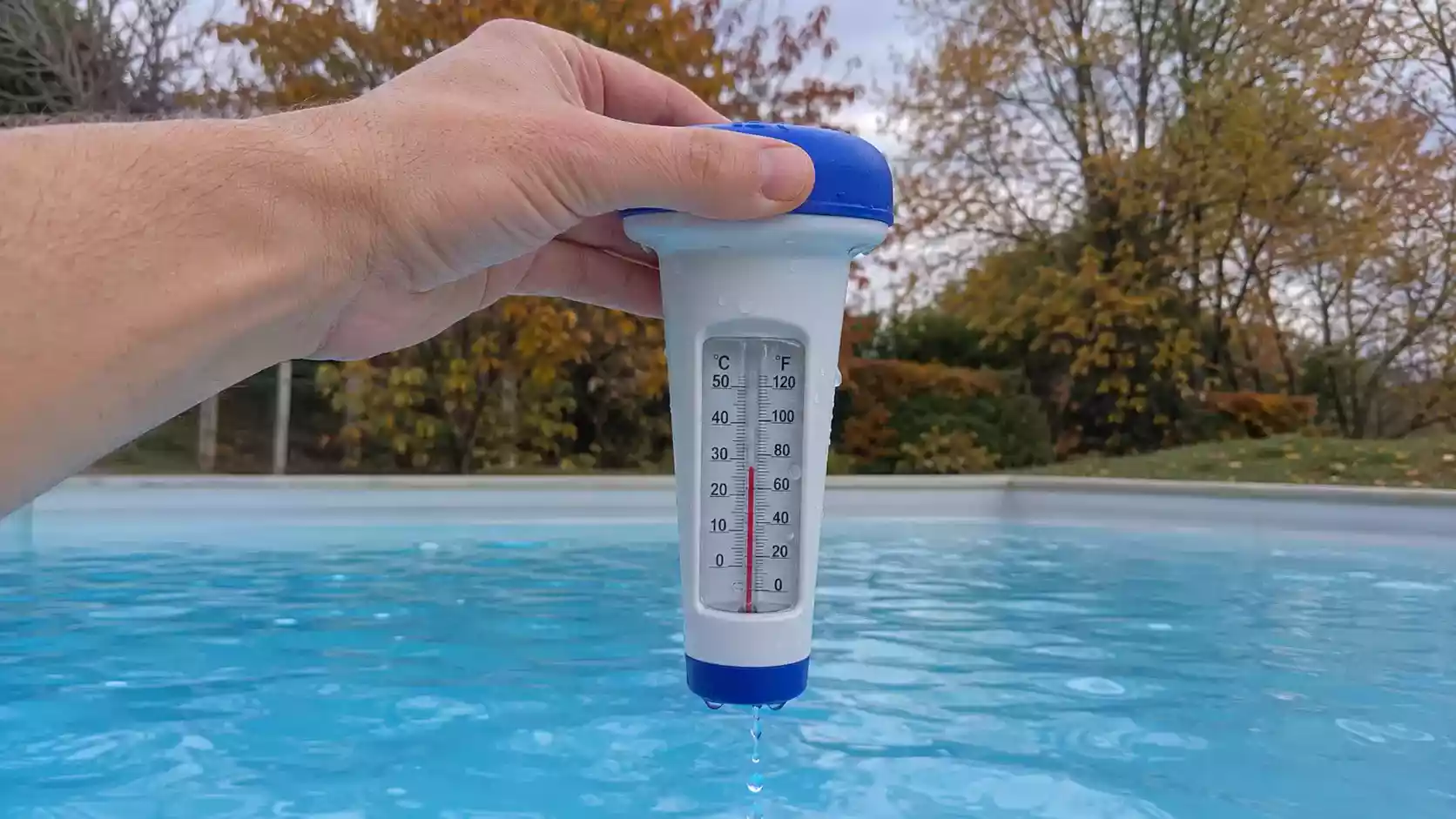 Main sortant un thermomètre flottant de l'eau d'une piscine en automne pour décider de l'hivernage