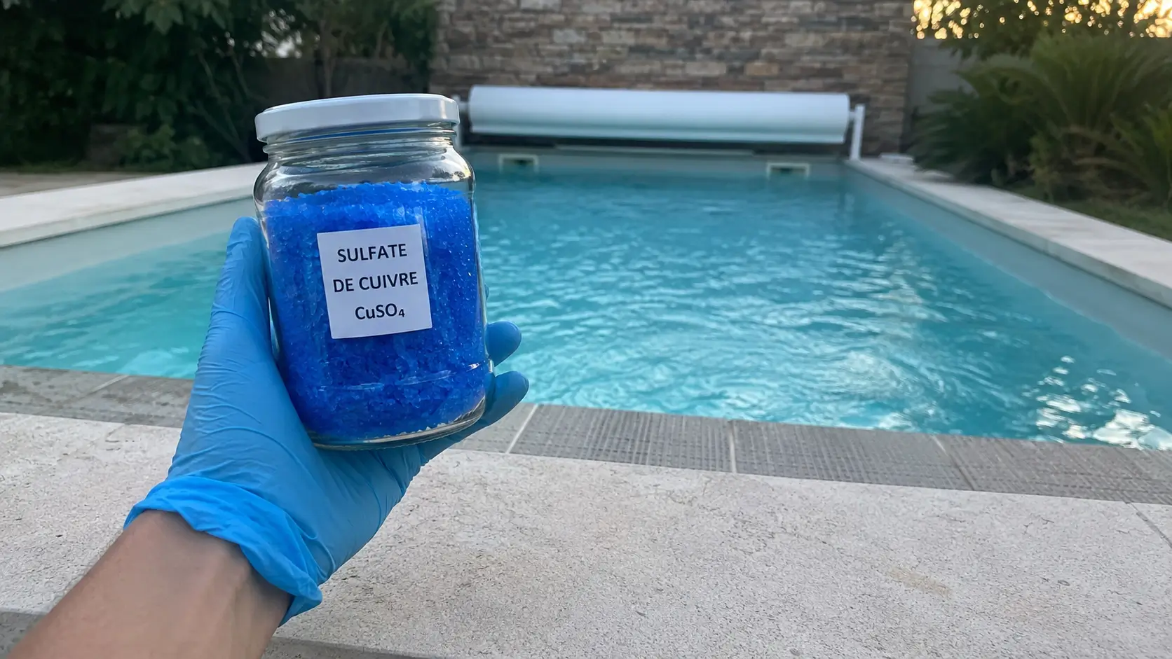 Cristaux bleus de sulfate de cuivre dans un pot en verre au bord d'une piscine