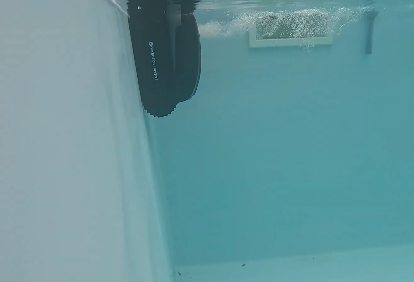 Le Wybot S2 nettoie une paroi de piscine, vu sous l'eau, skimmer en arrière-plan