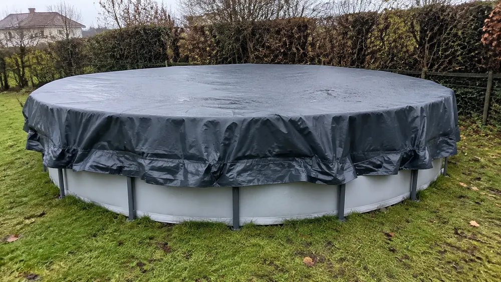 Bâche d'hivernage sombre couvrant une piscine hors sol ronde à paroi acier, retombée sur les côtés