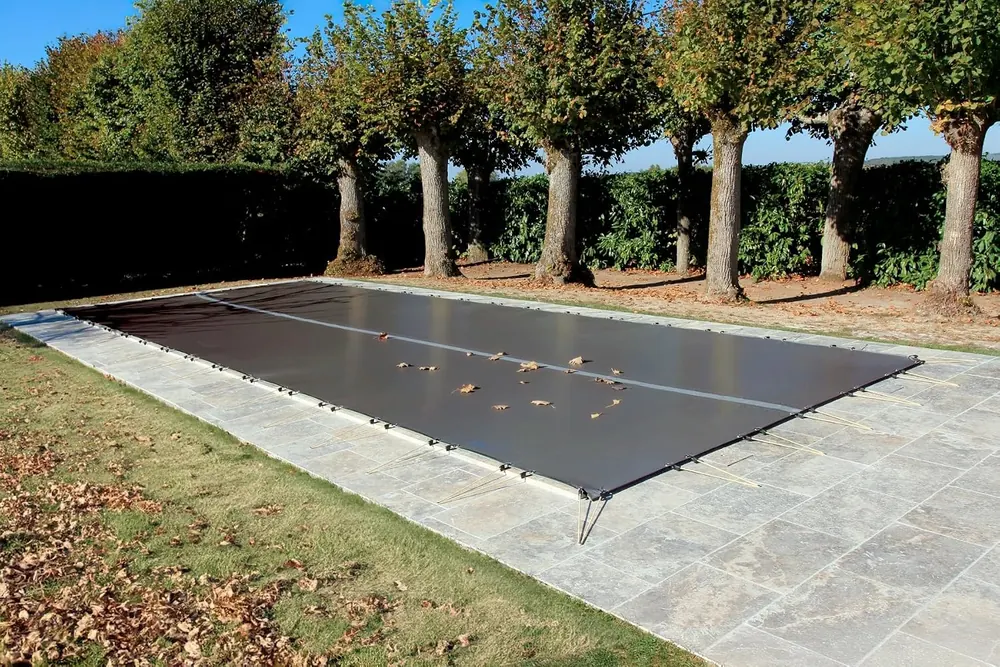 Bâche d'hivernage grise tendue par des sandows sur une piscine enterrée rectangulaire