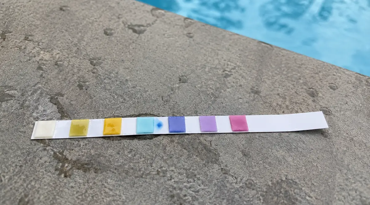 Bandelette de test pH posée sur la margelle d'une piscine après trempage