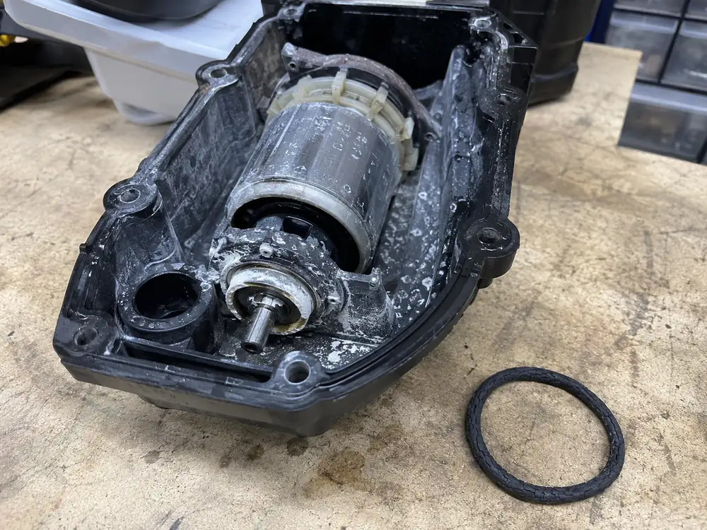 Bloc moteur de robot de piscine ouvert sur un établi, intérieur couvert de traces blanches de calcaire, avec un joint torique noir craquelé posé à côté