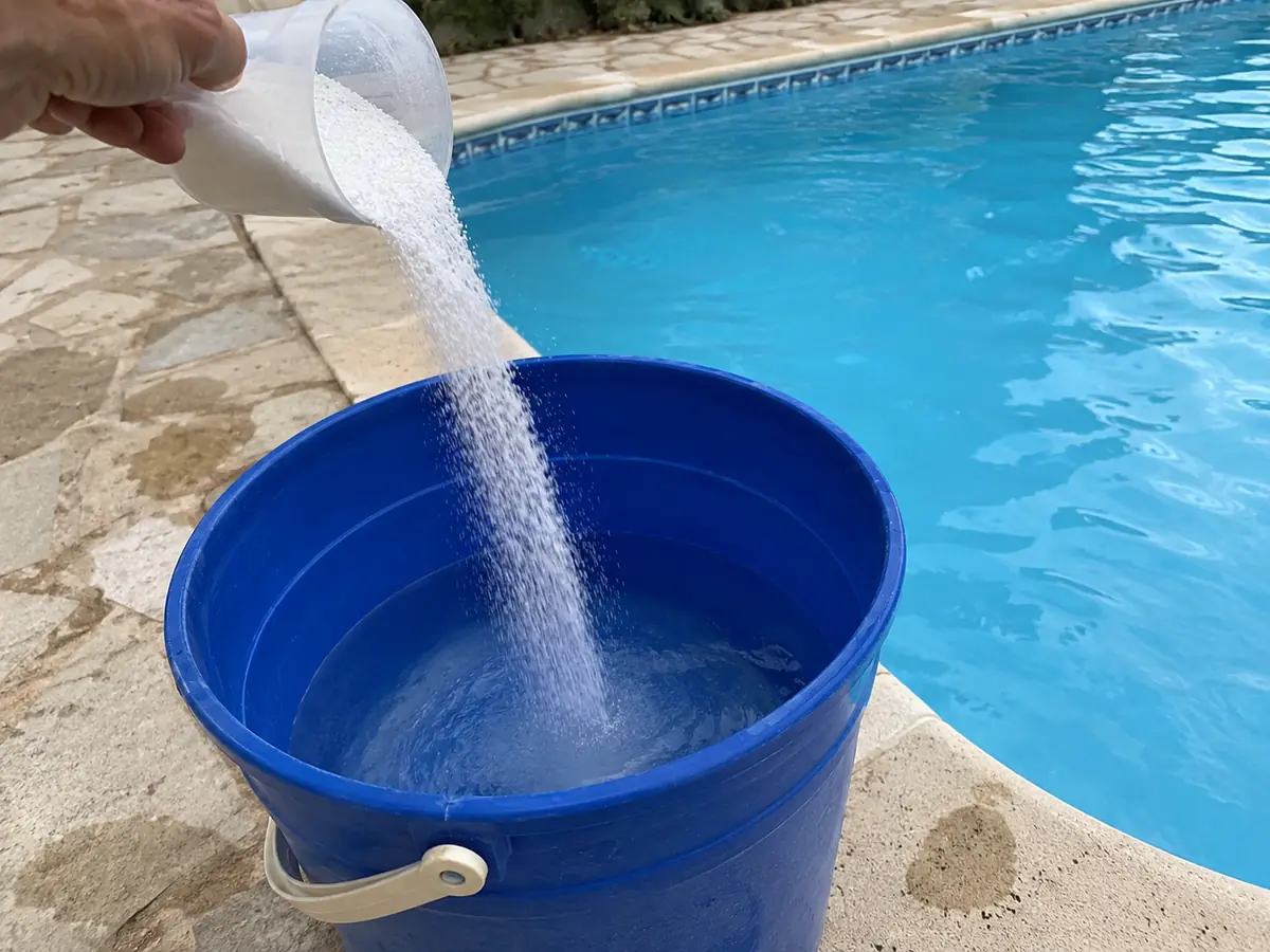 Poudre de pH moins versée depuis un gobelet doseur dans un seau d'eau au bord d'une piscine