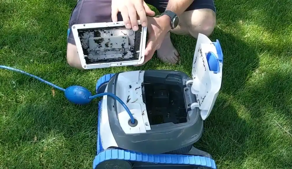 Panier filtrant du Dolphin S100 rempli de débris, sorti par le dessus du robot posé au sol