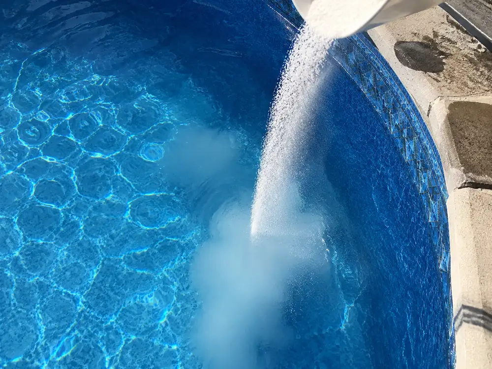 Poudre chimique versée directement dans une piscine formant un panache blanc dans l'eau