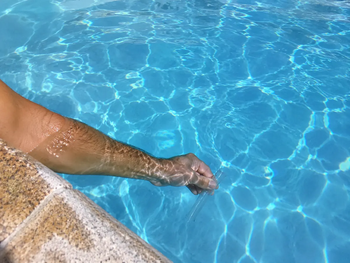 Bras plongé dans l'eau d'une piscine tenant un tube de prélèvement à 40 cm sous la surface