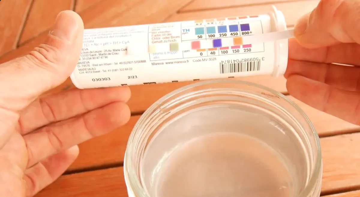 Bandelette d'analyse trempée dans un bocal d'eau de piscine et comparée à l'échelle du tube